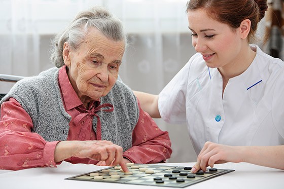 Smiling nurse playing board game with elderly lady