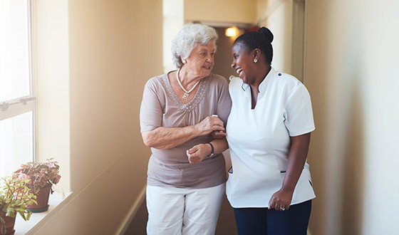 Elderly woman walking closely with nurse while laughing
