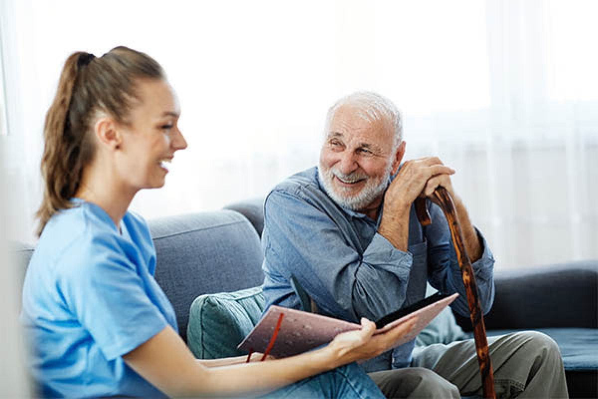 Elderly man on couch laughing with his nurse